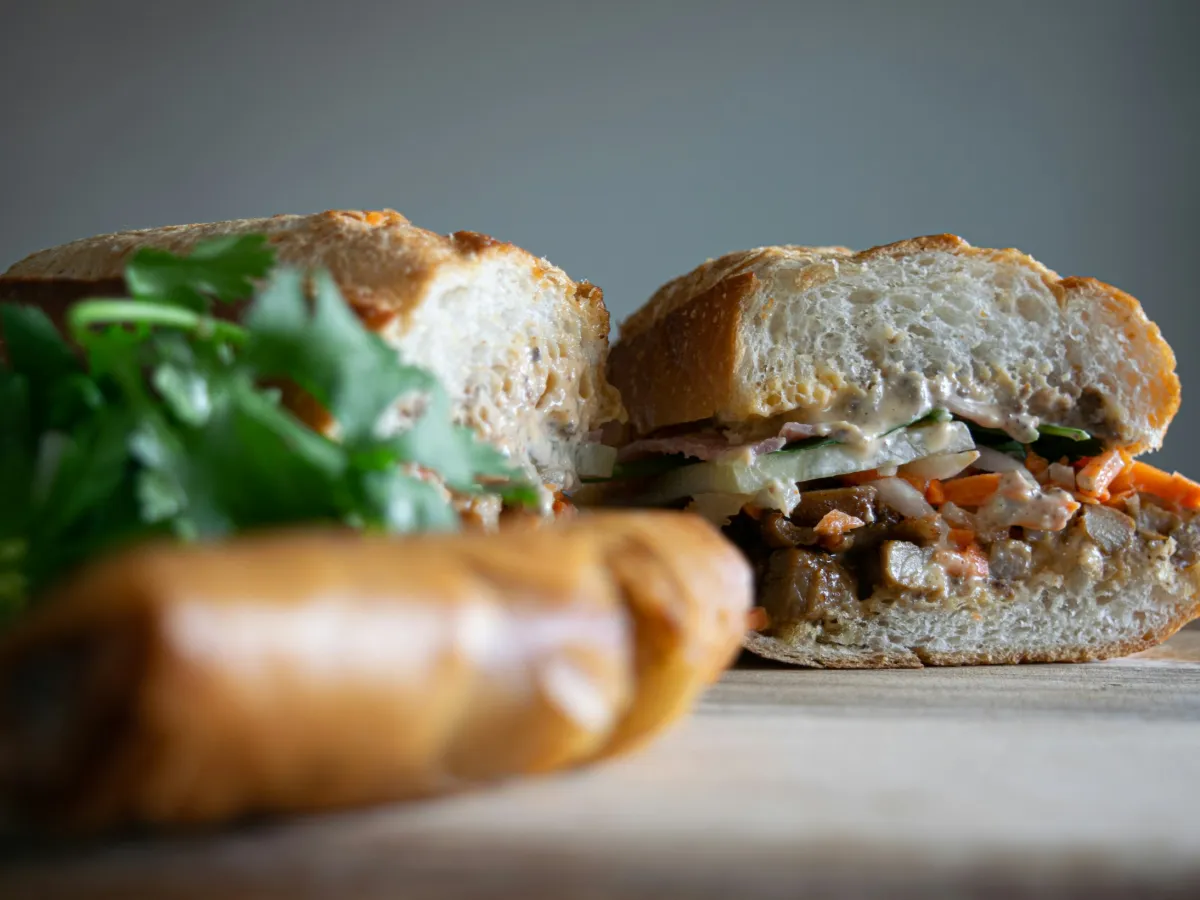 Ổ bánh mì kẹp thịt, rau thơm và đồ chua trên thớt gỗ