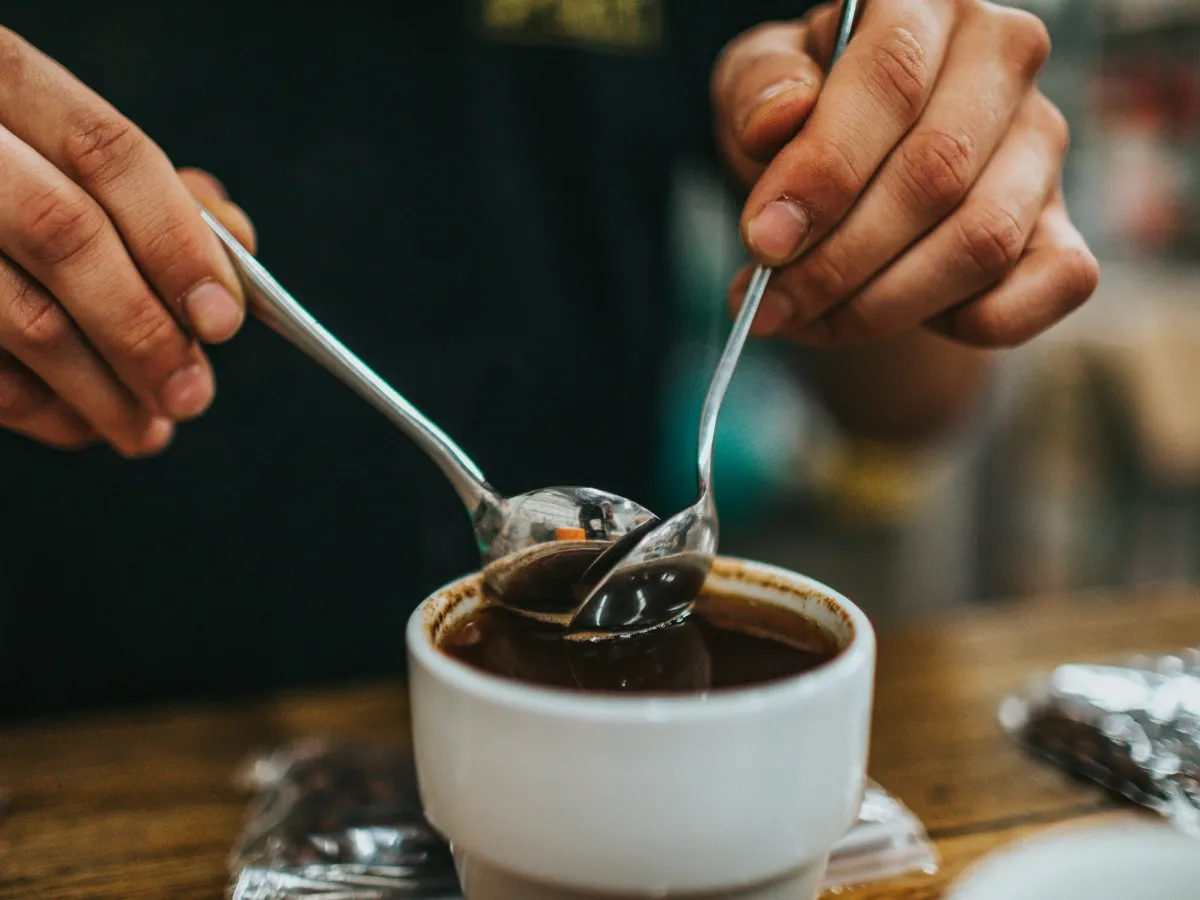 Hai bàn tay cầm thìa nếm cà phê trong chén sứ trắng ở buổi thử cà phê
