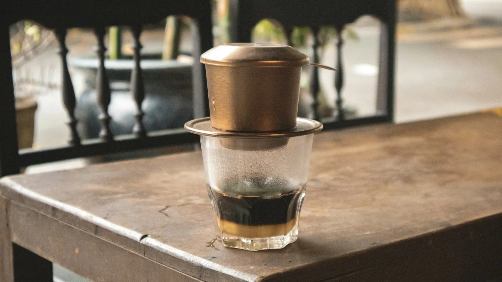 Phin cà phê bằng đồng nhỏ giọt trên ly thủy tinh đặt trên bàn gỗ, minh họa cho trang tra cứu đặt phòng Nâu Rẫy