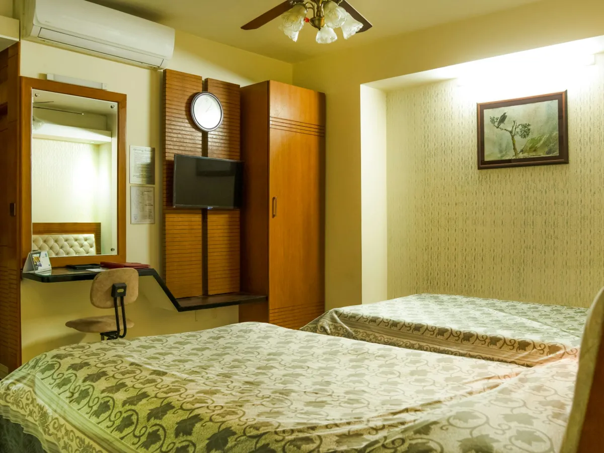 Phòng gia đình ở Buôn Ma Thuột: giường đôi và giường đơn trải khăn hoa văn, tủ gỗ, bàn trang điểm và TV treo tường