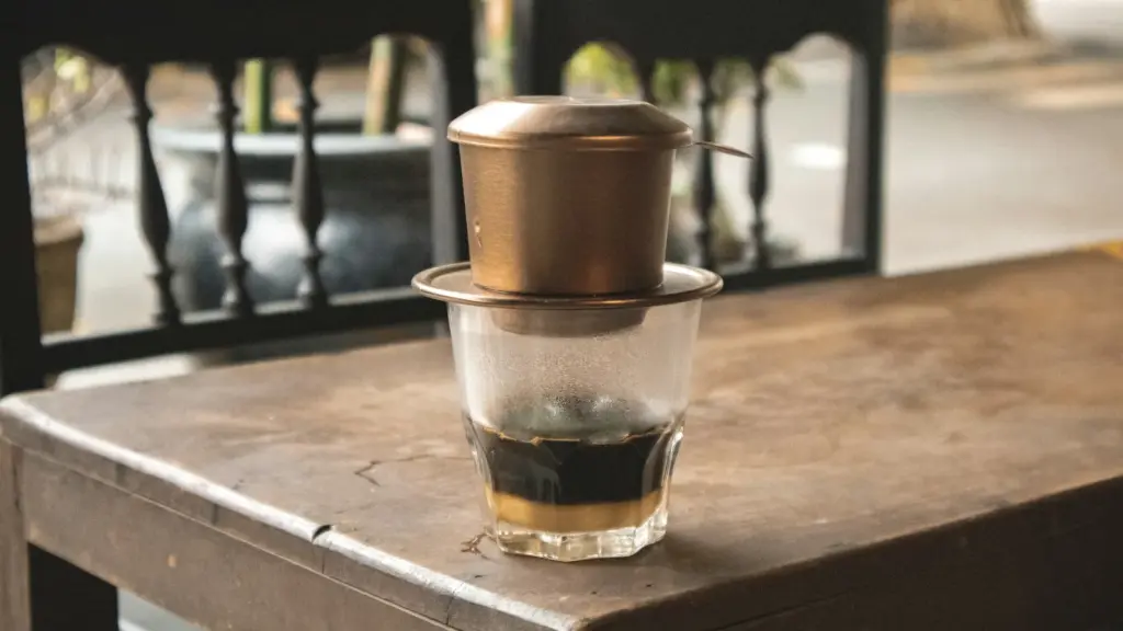 Phin đồng nhỏ giọt trên ly thủy tinh đặt trên bàn gỗ cũ, cách uống cà phê Buôn Ma Thuột quen thuộc nhất (ảnh minh họa)